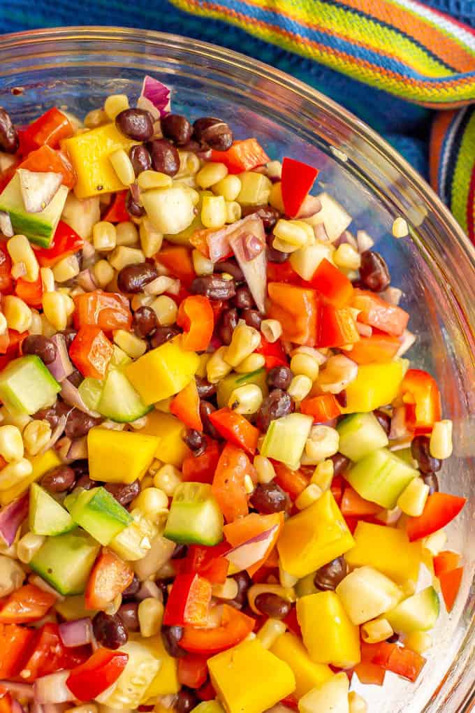 Close up of a colorful veggie mix with black beans and mango in a clear glass bowl