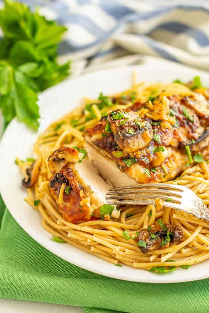 Roasted chicken with mushrooms, cheese and wine sauce over spaghetti noodles on a plate with a fork about to pick up a piece