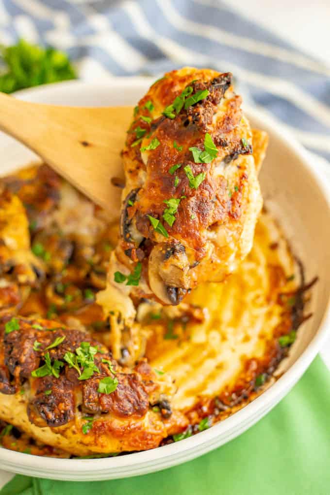 A roasted cheesy chicken breast being lifted out of a casserole dish