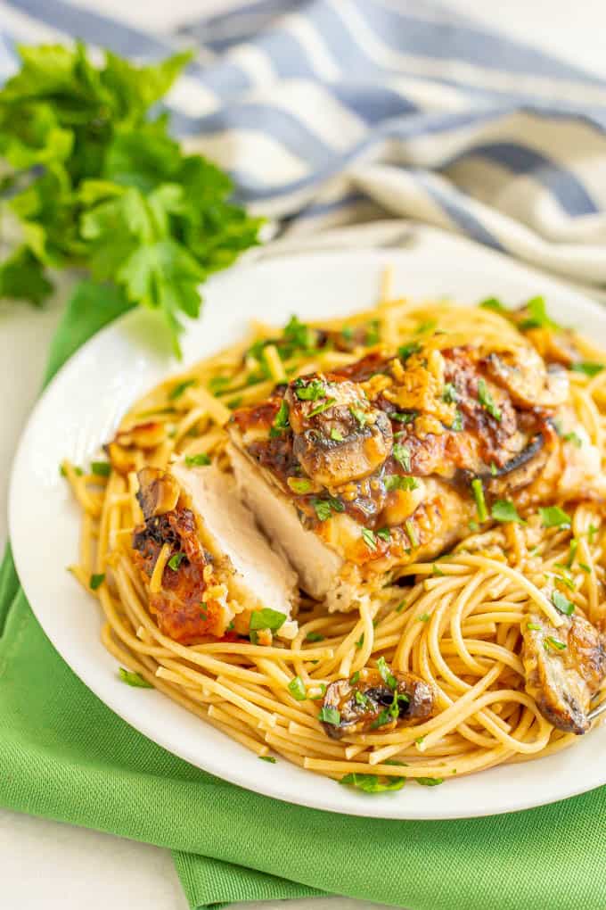 Roasted chicken with mushrooms, cheese and wine sauce over spaghetti noodles served on a white plate