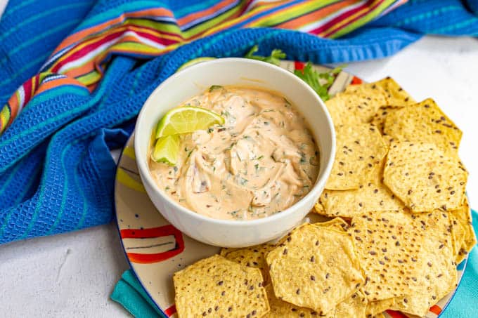 A creamy adobe chili yogurt dip in a bowl on a plate filled with tortilla chips
