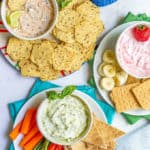 Three bowls with different Greek yogurt dips arranged on plates with various fruit, veggies and other dippers and a text box on top