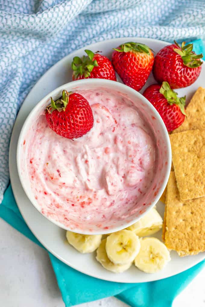 Strawberry yogurt dip in a white bowl served with fresh fruit and graham crackers