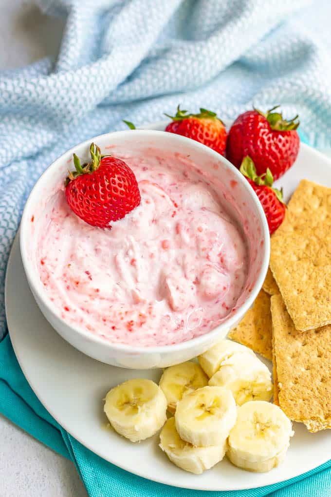 A fruity yogurt dip in a white bowl served with fresh fruit and graham crackers