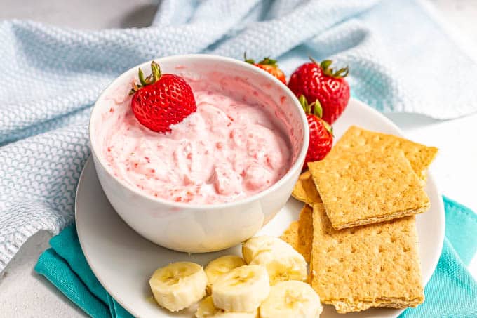 A fruity pink yogurt swirled dip in a white bowl served with fresh fruit and graham crackers