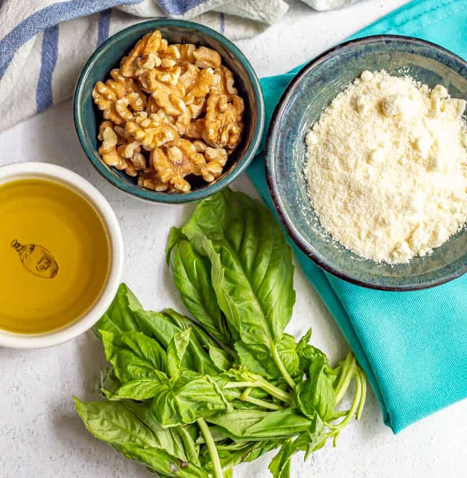 Ingredients needed for homemade basil pesto in separate bowls on a marble counter