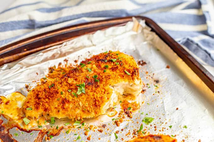 A baked Parmesan crusted chicken breast on a sheet pan lined with aluminum foil