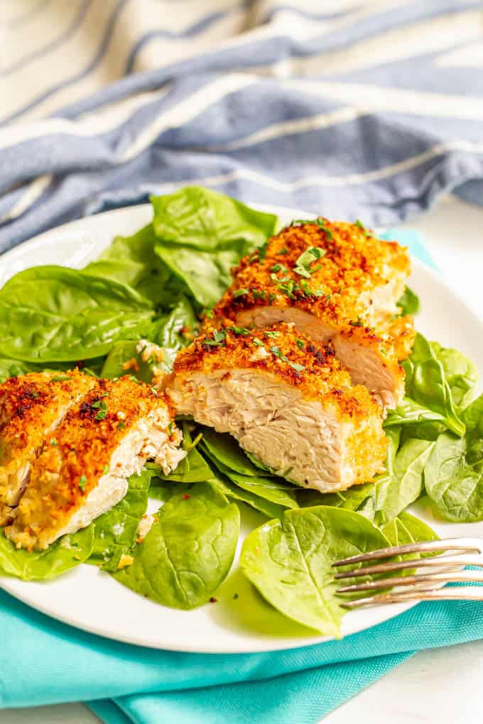 A close up of sliced crunchy baked chicken over baby spinach