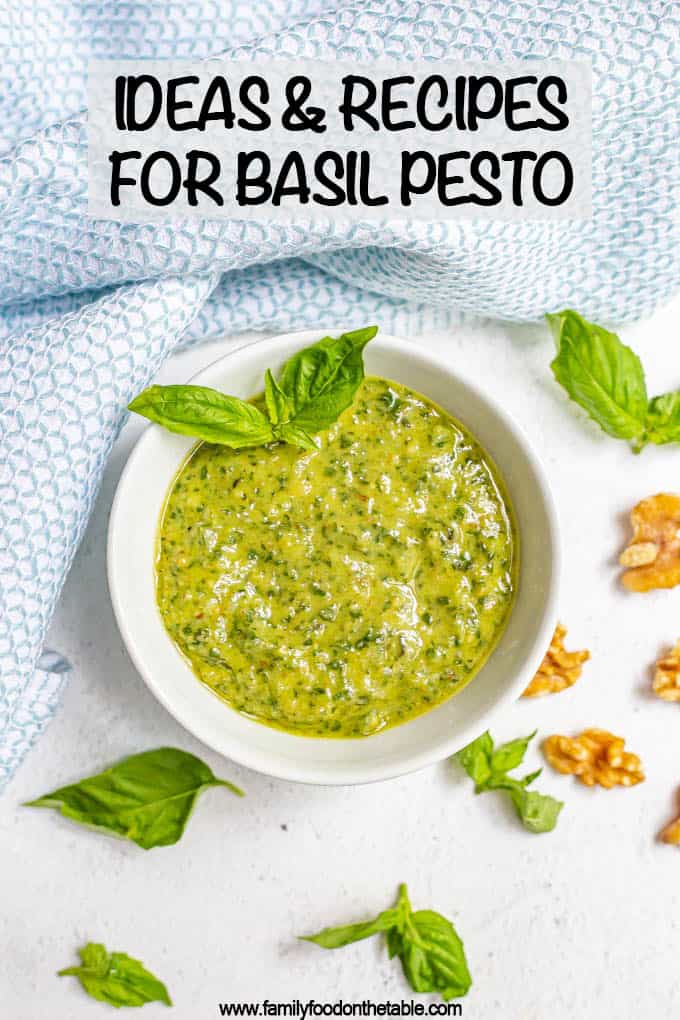 A white bowl of fresh basil pesto with sprigs of fresh pesto and walnut pieces scattered nearby