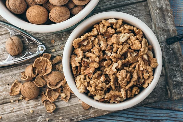 Shelled walnuts in a bowl beside a bowl of walnuts in the shell