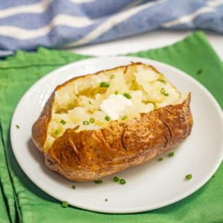 A crispy baked potato with butter and chives on a small white serving plate on top of green napkins