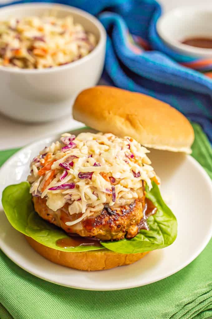 A turkey burger on bun on a white plate with coleslaw on top