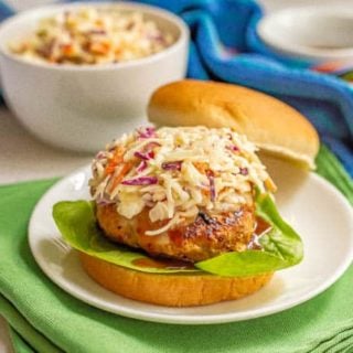 A turkey burger with coleslaw on a white plate on green napkins