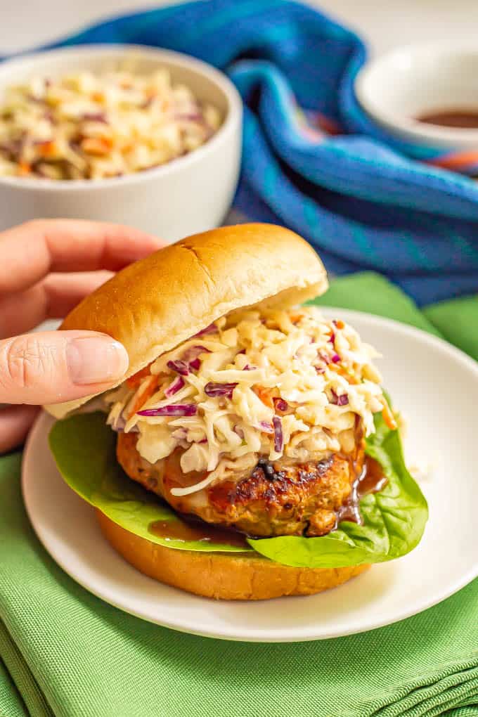 A burger bun top about to be placed on top of a BBQ turkey burger topped with slaw