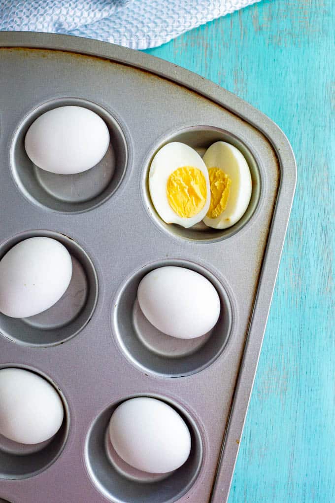 Eggs in a muffin tin with one hard boiled egg cut open in half