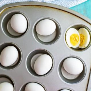 Cooked white eggs in a muffin tin with one cut open in half
