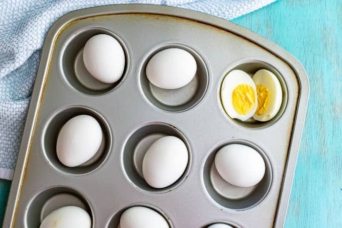 Cooked white eggs in a muffin tin with one cut open in half