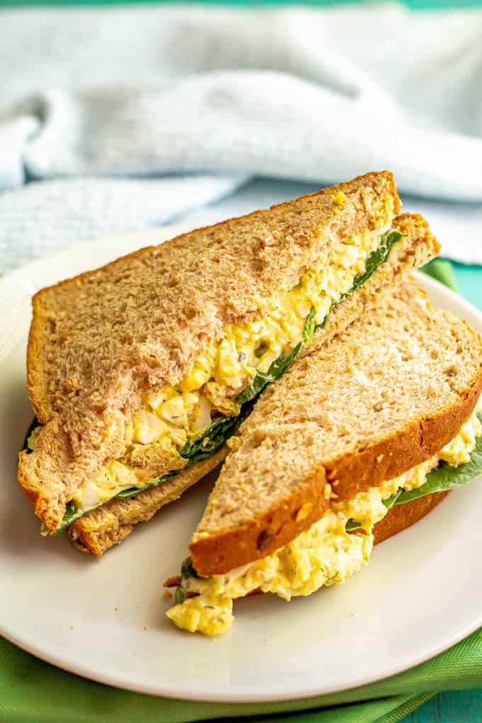 An egg salad sandwich with spinach cut in half and stacked on a white plate