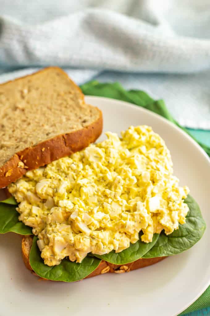 Egg salad piled on a bed of spinach on the bottom half of a sandwich