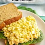 Egg salad piled on a bed of spinach on the bottom half of a sandwich with a text overlay on the photo