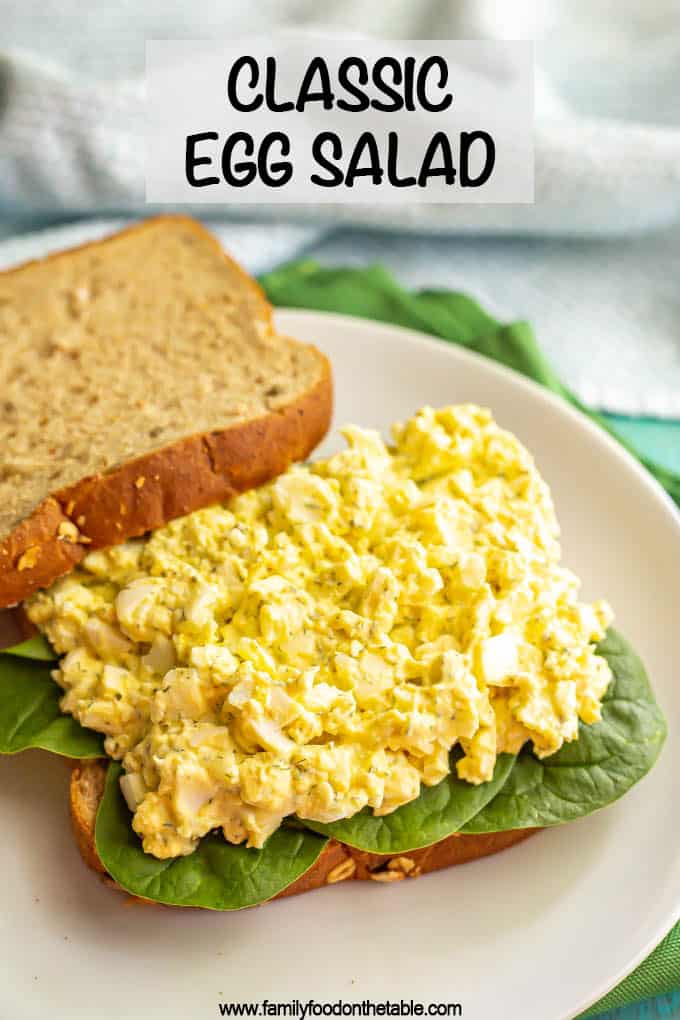 Egg salad piled on a bed of spinach on the bottom half of a sandwich with a text overlay on the photo