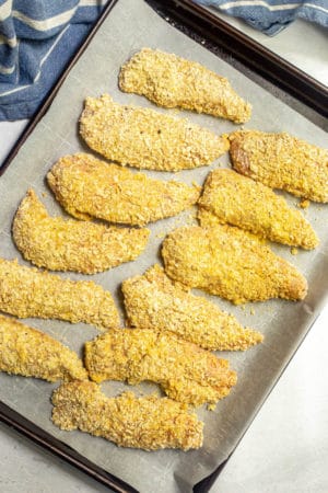 Coated chicken tenderloin pieces on a baking sheet before being cooked