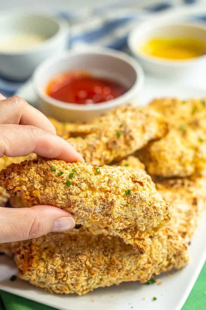 A hand picking up a crusted chicken tender from a large platter