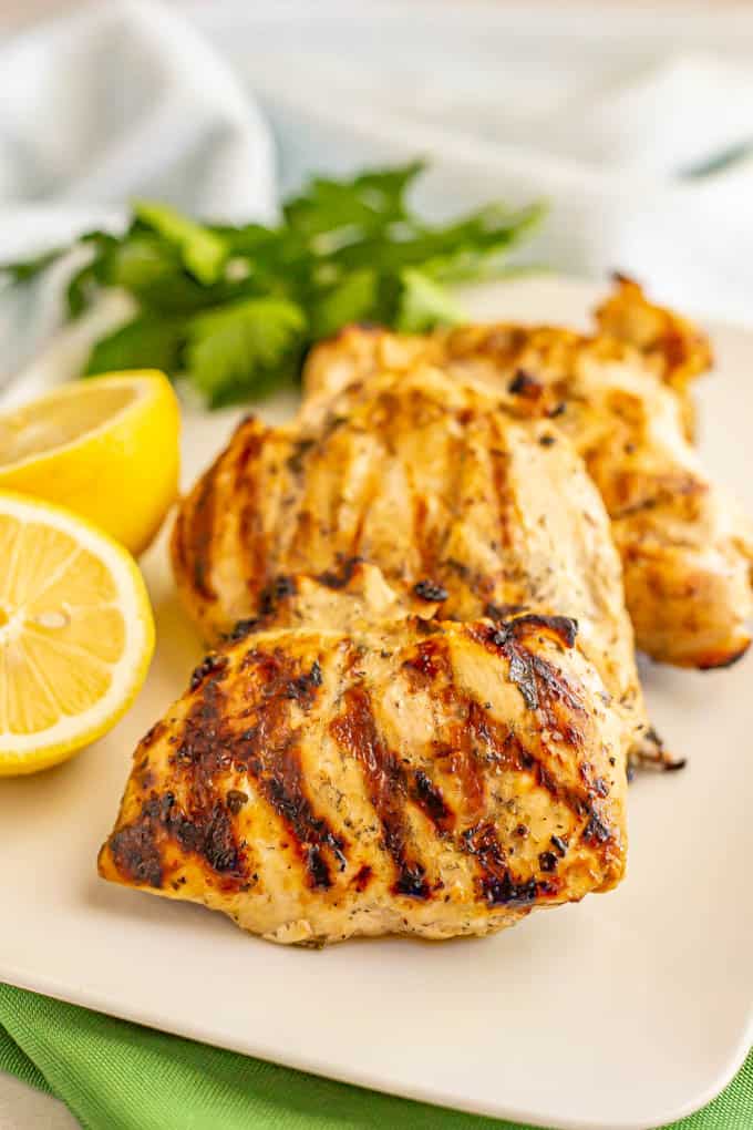 Grilled chicken breasts on a white serving platter with parsley and lemon as garnishes