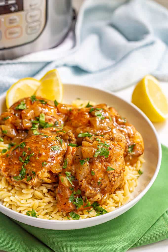 Chicken thighs served over orzo pasta in a white bowl with a brown sauce and parsley on top