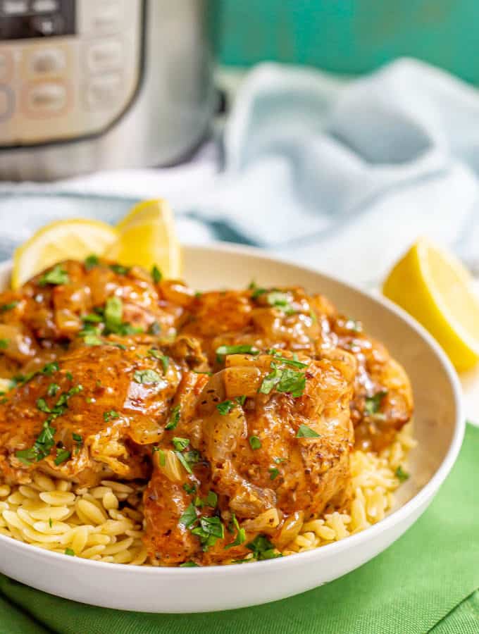 Chicken thighs served over orzo pasta in a white bowl with a brown sauce and parsley on top and an Instant Pot in the background