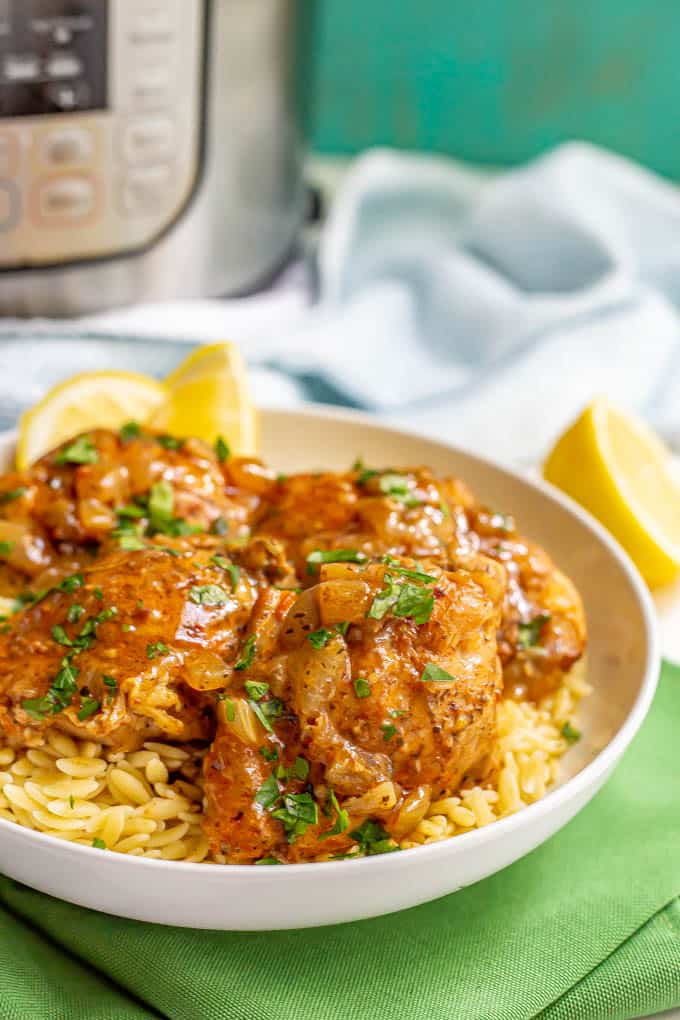 Chicken thighs served over orzo pasta in a white bowl with a brown sauce and parsley on top and an Instant Pot in the background