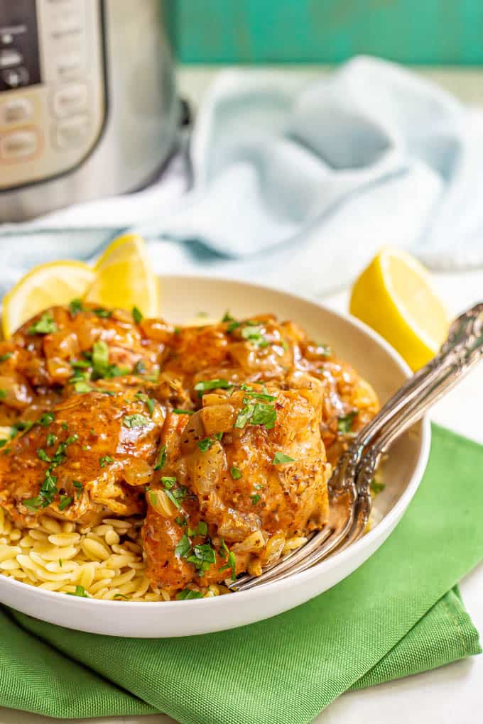 Chicken thighs served over orzo pasta in a white bowl with a brown sauce and parsley on top and two forks tucked in