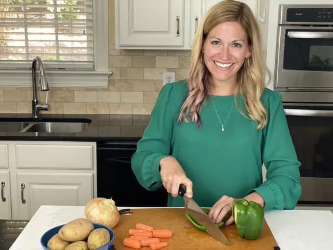 A woman slicing a green bell pepper on a cutting board in a kitchen