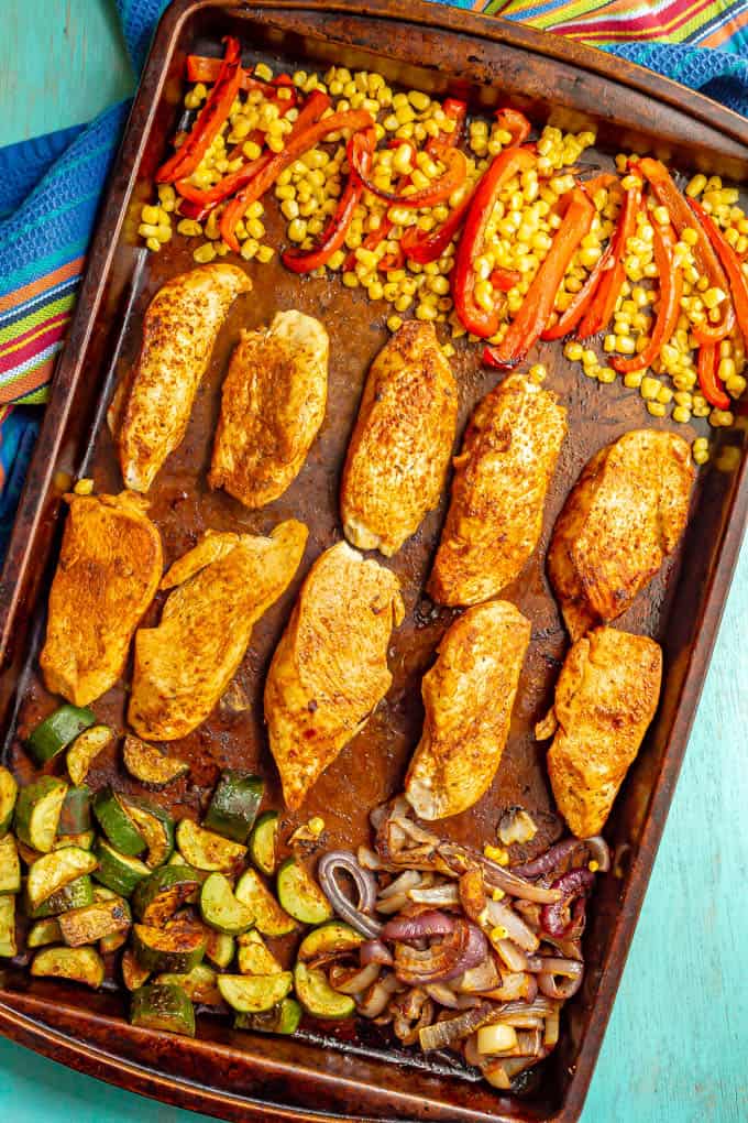 A baking sheet with cooked seasoned chicken strips and roasted vegetables