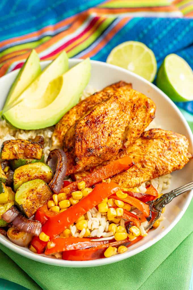 A fork tucked into a large white bowl of chicken and veggies over steamed brown rice