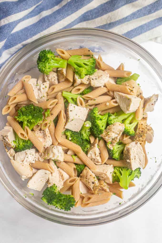 Pasta, cooked chicken and broccoli mixed together in a large glass bowl