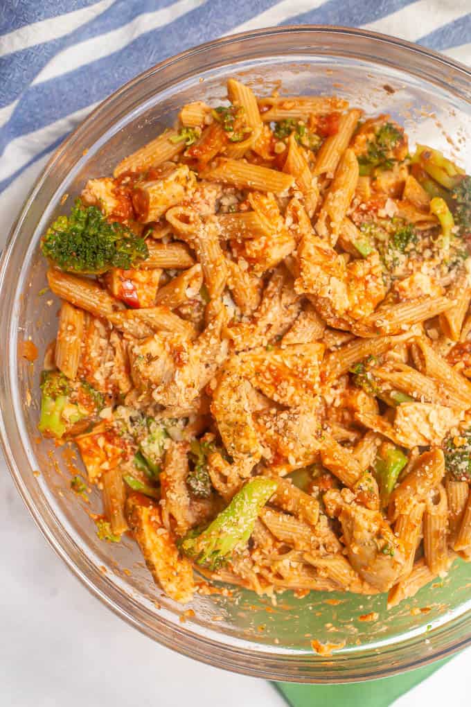 A glass mixing bowl with pasta, chicken and broccoli plus a tomato sauce