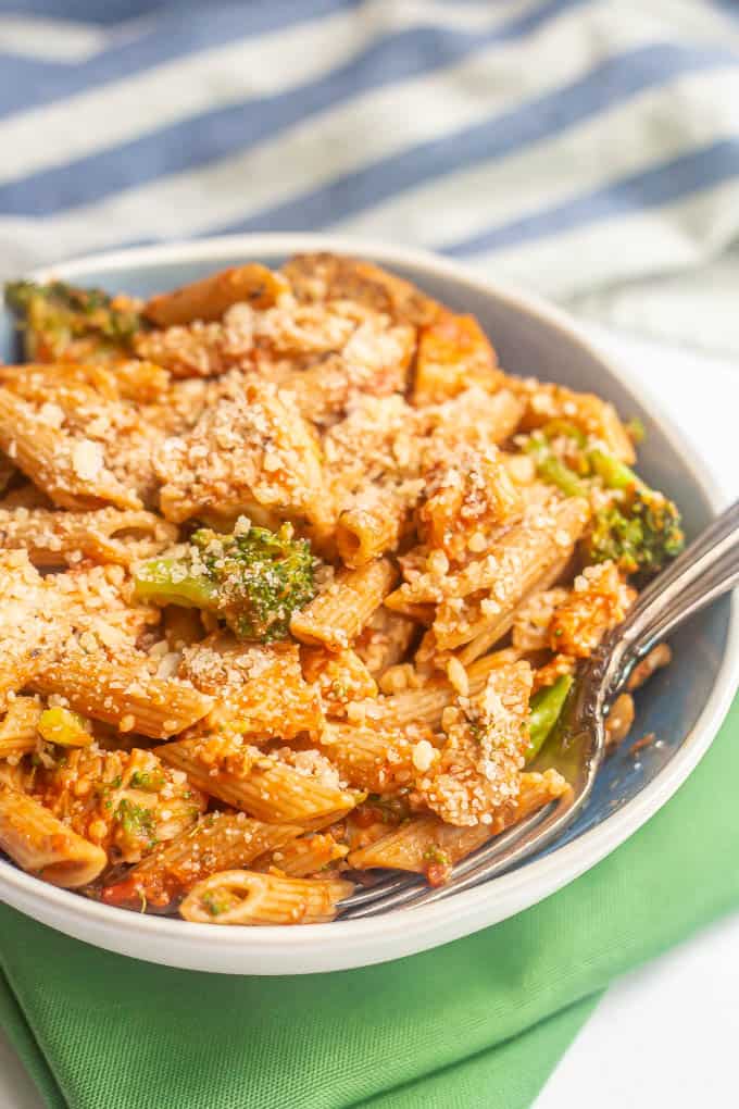 A large blue and white bowl with penne pasta, chicken and broccoli coated in marinara and Parmesan cheese