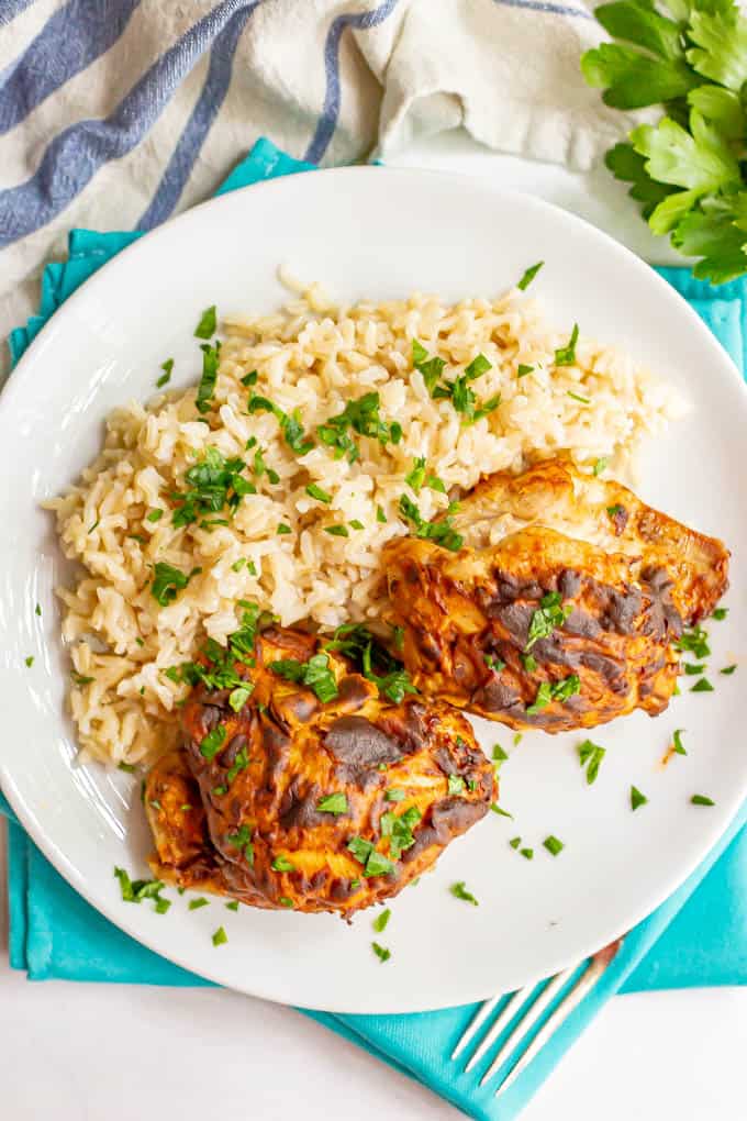 Browned chicken thighs served with rice and parsley on a white dinner plate