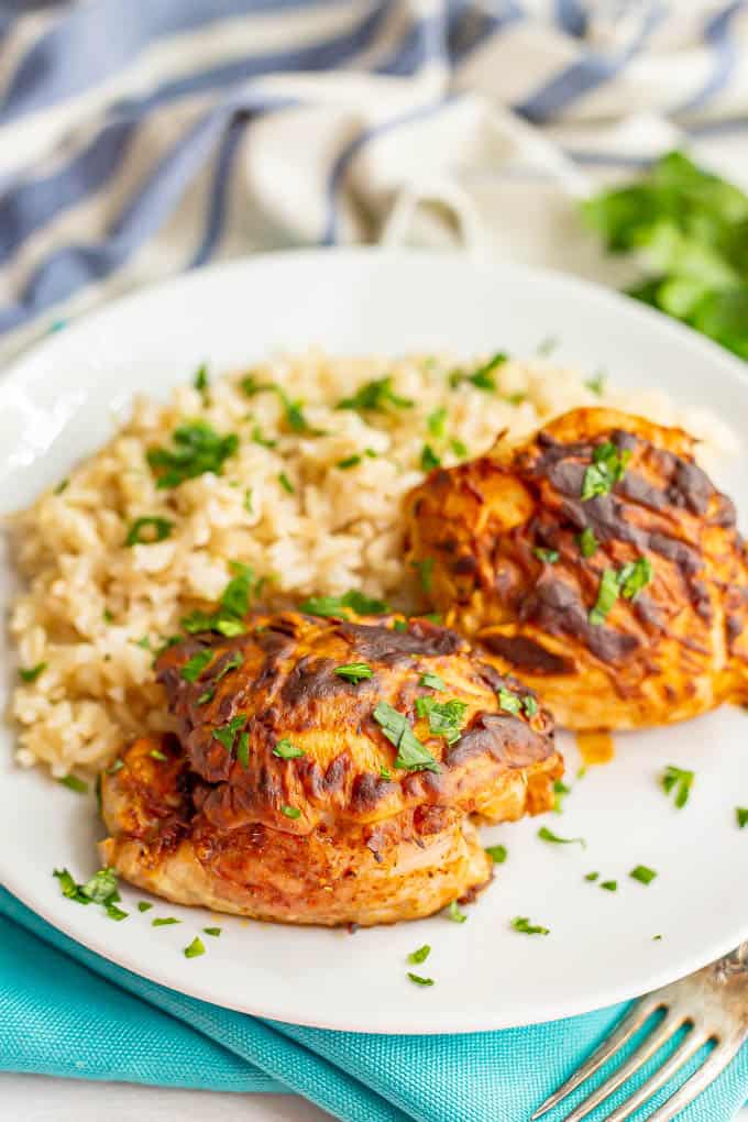 Browned chicken thighs served with rice and parsley on a white dinner plate