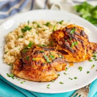 Browned chicken thighs served with rice and parsley on a white dinner plate