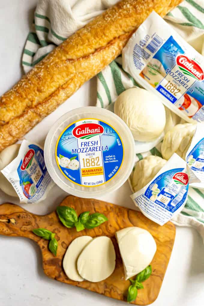 A display of different sizes and types of fresh mozzarella, plus sprigs of a basil and a long French baguette