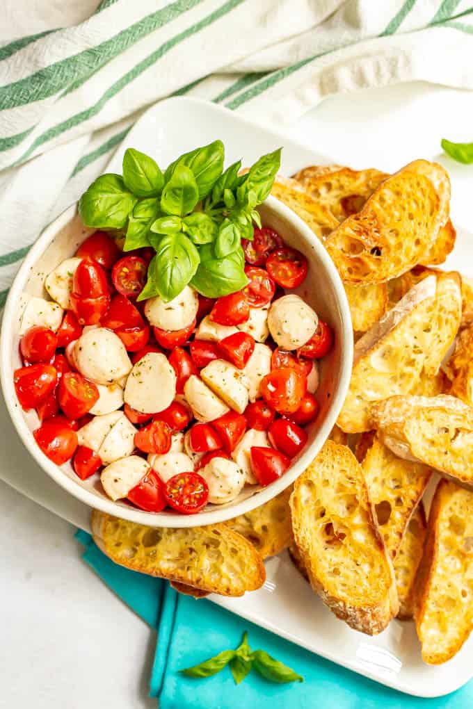 A bowl full of bruschetta toppings on a plate of toasted baguette slices
