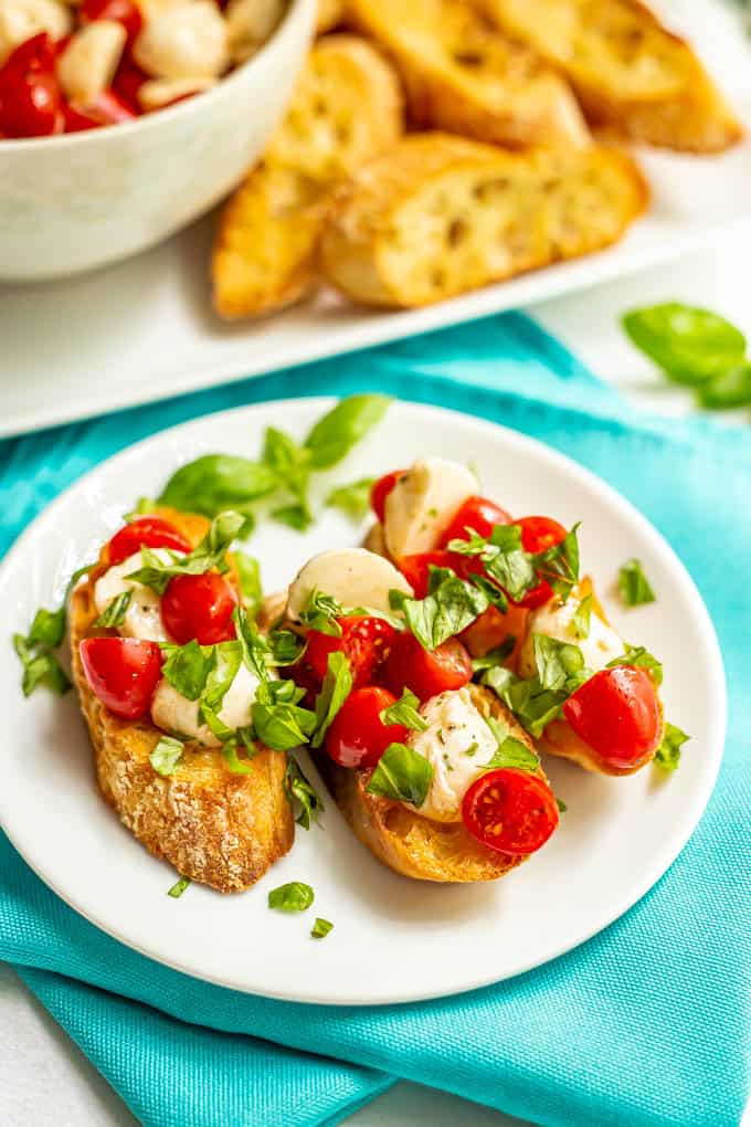 Bruschetta slices with tomatoes, mozzarella and basil on a small white plate