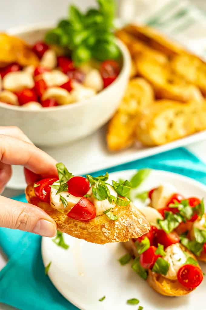 A piece of bruschetta being picked up from a small serving plate