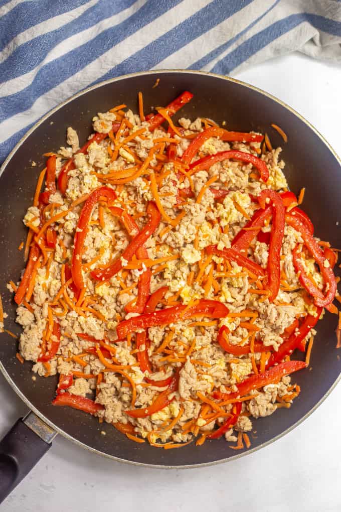 Ground chicken mixed with red bell peppers, carrots and eggs in a large skillet