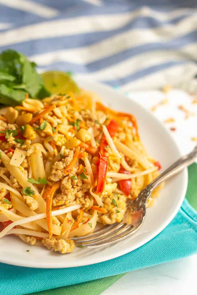 Chicken pad Thai plated on a white dish with a fork with a garnish of cilantro, lime and peanuts