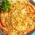 Chicken pad Thai with rice noodles in a large skillet topped with peanuts, cilantro and lime wedges and a text box overlay on the photo