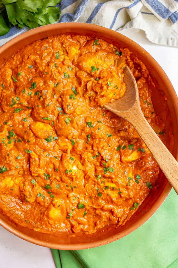 A large skillet with a wooden spoon picking up some chicken tikka masala