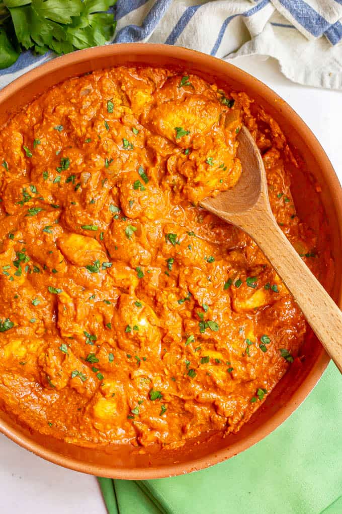 A large skillet with a wooden spoon picking up some chicken tikka masala